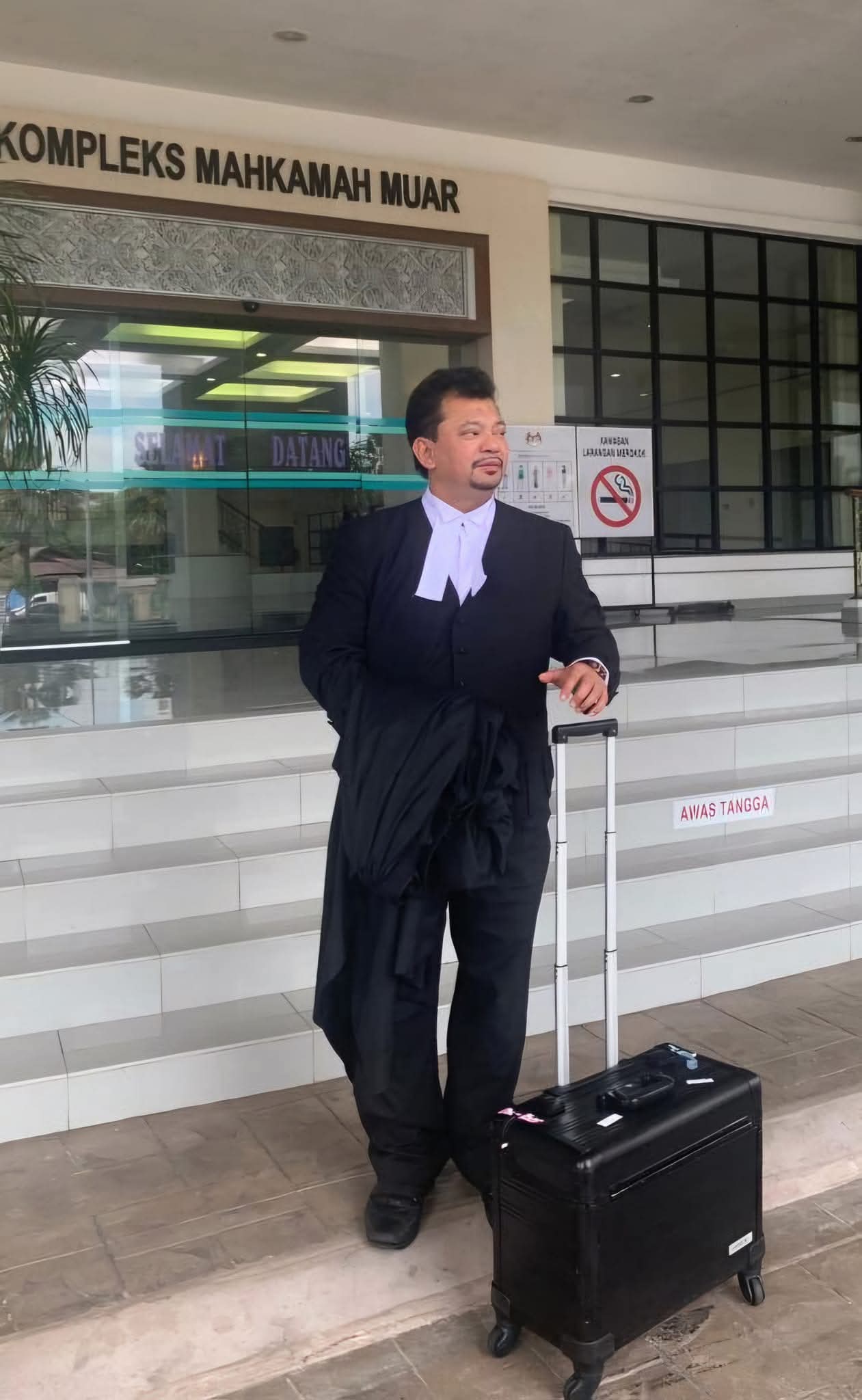 An advocate in court dress arriving with a trial case at the Muar court complex.